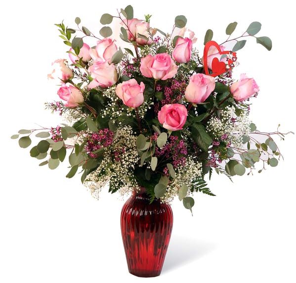 Twelve beautiful pink roses decorated with greenery and baby's breath arranged in a glass vase.