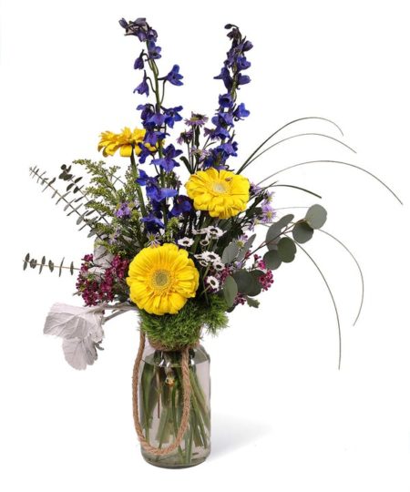 A vase of beautiful long lasting wild flowers to bring the outdoors indoors. This milk bottle style vase contains mini-gerbera daisies, bear grass, and golden aster among its assortment.