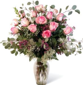 Twelve beautiful pink roses decorated with greenery and baby's breath arranged in a glass vase