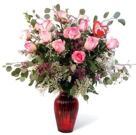 Twelve beautiful pink roses decorated with greenery and baby's breath arranged in a glass vase. 