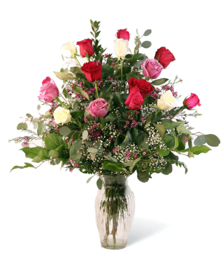 Twelve beautiful multi-colored mixed roses decorated with greenery and baby's breath arranged in a glass vase. Premium option also includes purple waxflower. 